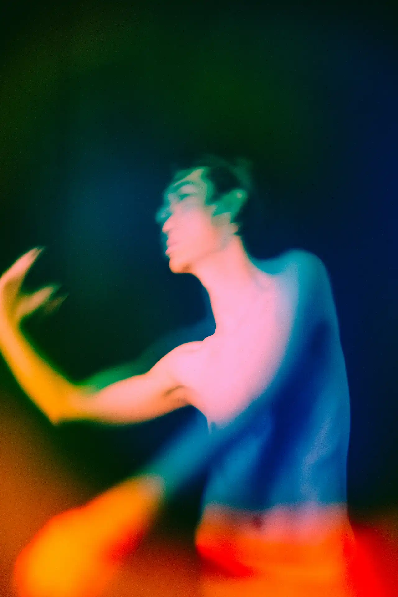 A dancer in motion, blurred and lit in green, blue, and orange light